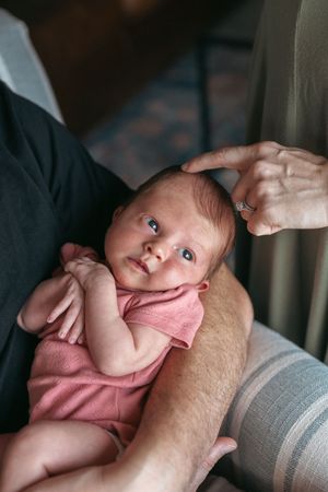 A series of photos showing a baby in a pink outfit lying on a gray surface while being gently touched.