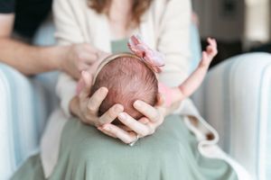 A person holds a small baby's hand while resting on a light-colored blanket.