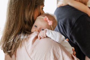A tender moment between parent and newborn baby dressed in white against a soft background.