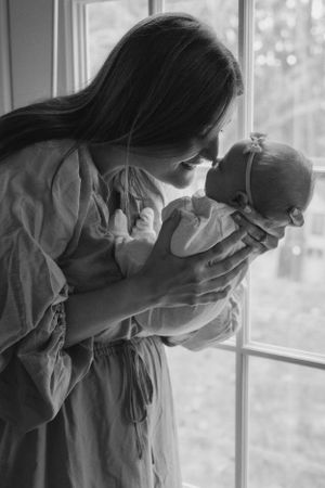 Silhouette of parent holding infant by window in black and white photograph.