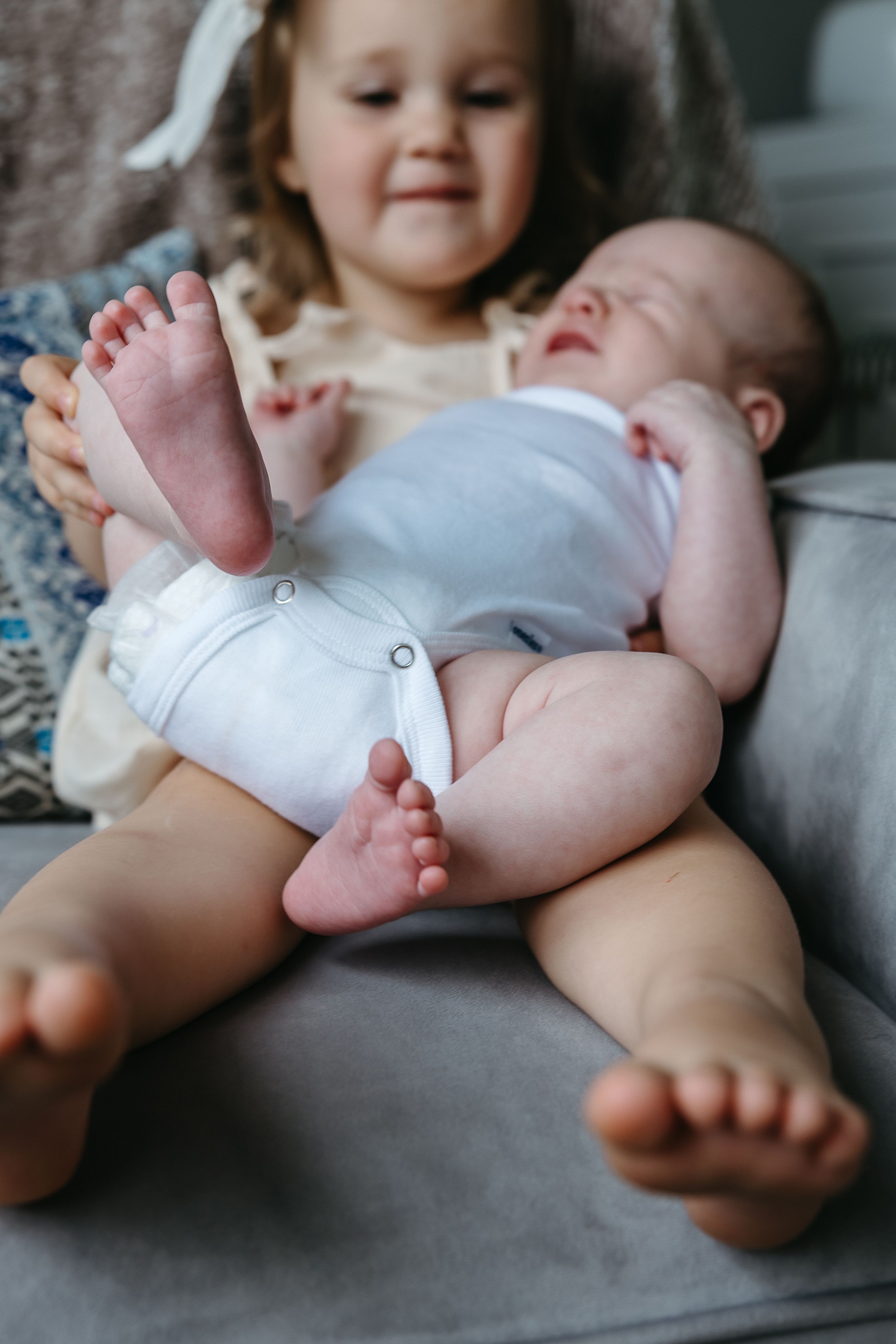 Close up of a newborn baby's feet with their sibling sitting beside them.