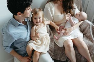 A family sits close together on a couch, sharing a tender moment with their young children.