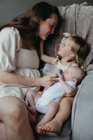 A tender family moment captured on a gray couch as two young children share quality time with their parent.