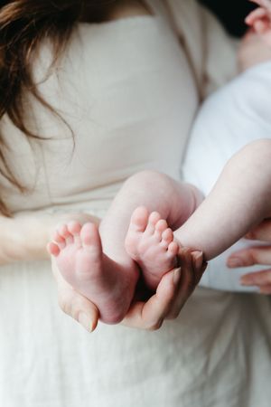 Close-up of tiny baby feet being gently cradled in adult hands against white fabric background.