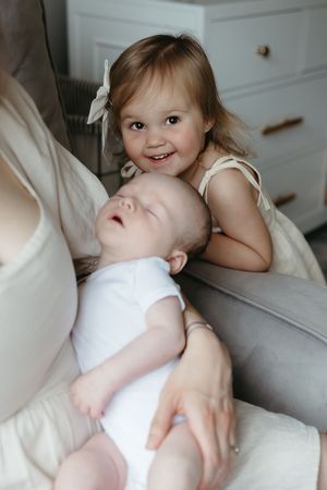 Two children in white clothing on a couch, with one resting and the other smiling at the camera.