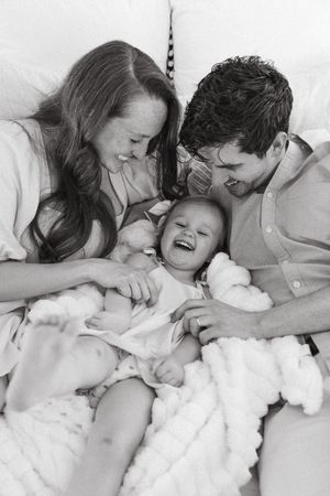 A heartwarming black and white photo of a joyful family moment as they share laughter while lying on a bed together.
