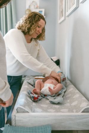 A baby lies on a changing table while being changed in a white nursery setting during a diaper change.
