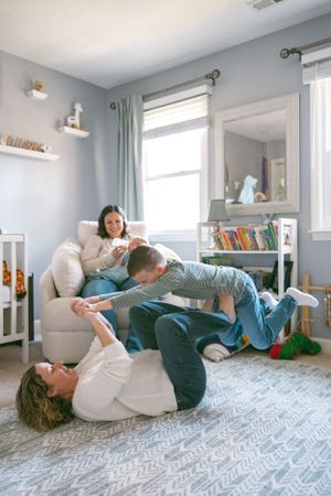 A family relaxes together in a cozy gray living room with white shelving and mint green curtains.