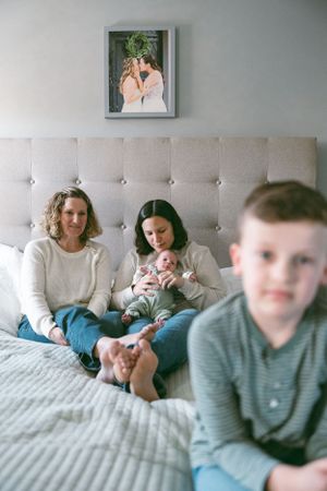 A casual family moment on a gray tufted headboard bed with a framed photograph displayed on the wall above.