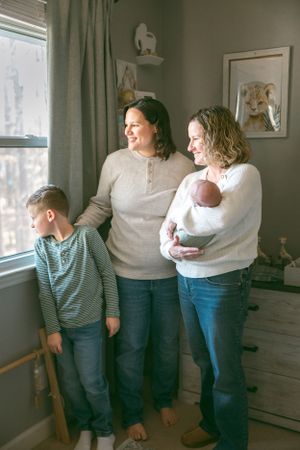 A family stands together by a window in a cozy nursery decorated with animal artwork on the walls.