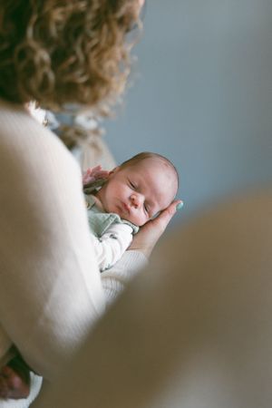 A tender moment shows a sleeping baby being cradled in gentle arms against a soft white sweater.