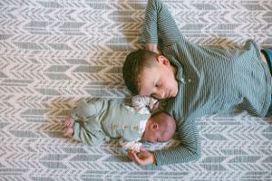 Two people lying together on a gray and white chevron patterned rug, wearing matching light colored outfits.