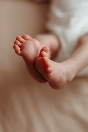 Close up macro shot of tiny newborn baby feet against soft beige background in gentle natural lighting.