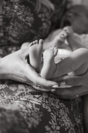 A close-up black and white photograph of tiny baby feet resting on adult hands against a patterned fabric background.