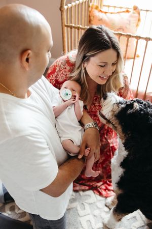 Couple in casual attire spending time with their fluffy black dog and baby on a comfortable rug.