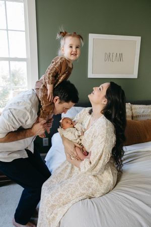 Happy family moment captured on bed with green wall and DREAM artwork in background.