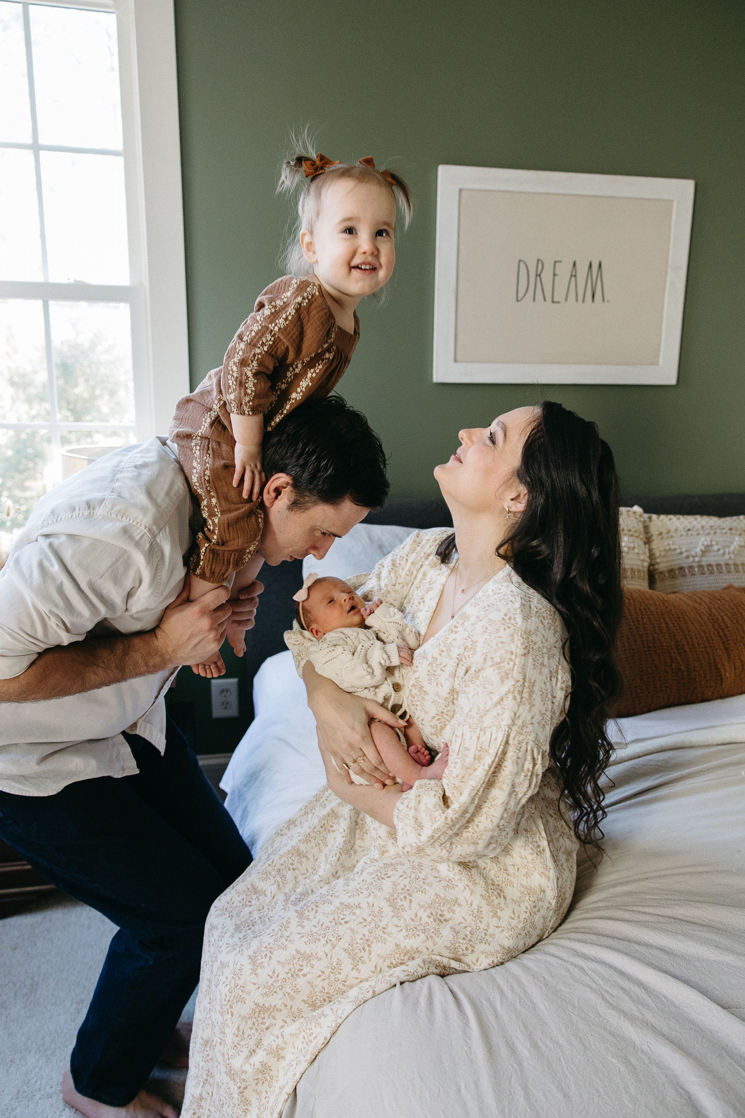 Happy family moment captured on bed with green wall and DREAM artwork in background.