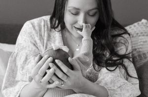 A person in a white sweater lies on a bed texting on a mobile phone in black and white photography.
