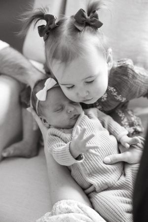 A tender black and white portrait of two small children wearing hair bows as they share a sweet moment together.