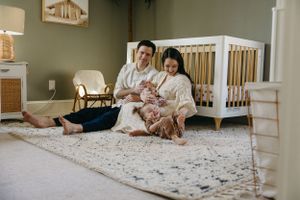 Two people sitting on a plush carpet beside a white wooden crib in a cozy nursery bedroom.