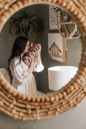View through woven rattan mirror shows cozy interior with hanging plants and neutral decor in warm natural tones.