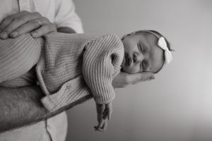 A sleeping baby in a cozy knit sweater is cradled in someone's arms in black and white.