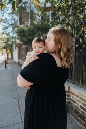 A tender moment between parent and infant against a natural outdoor backdrop with trees.
