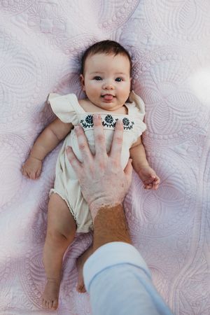Infant in white romper lying on textured blanket as hand reaches to place decorated stickers.