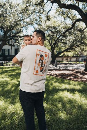 A loving moment shared outdoors beneath blooming trees while wearing a playing card design t-shirt on a sunny day.
