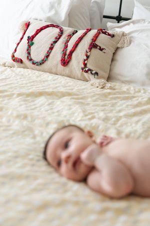 Decorative pillow with the word 'Love' spelled out in red and green beads on white bedding.