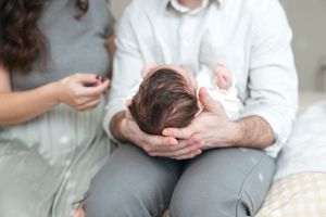 A newborn baby rests in gentle hands while being photographed during a tender family moment.