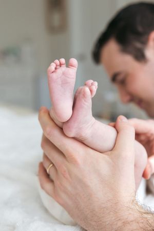 Close-up of tiny baby feet being gently held by adult hands on white bedding.