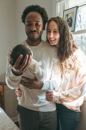 A couple smiles together while holding a bowling ball in a cozy home setting.