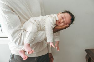 A sleeping baby wearing white clothing rests peacefully on someone's shoulder.