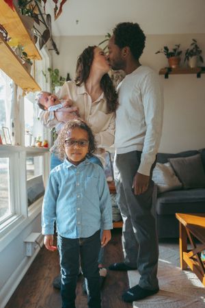A cozy family moment in a sunny living room with plants on shelves and wooden floors.