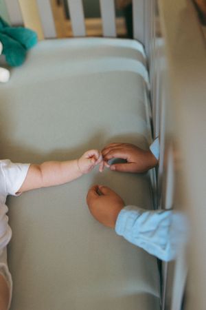 Two small hands reach towards each other in a tender moment against a soft grey background.
