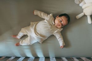 Baby wearing white clothing lies on plush blue surface with a cheerful expression.