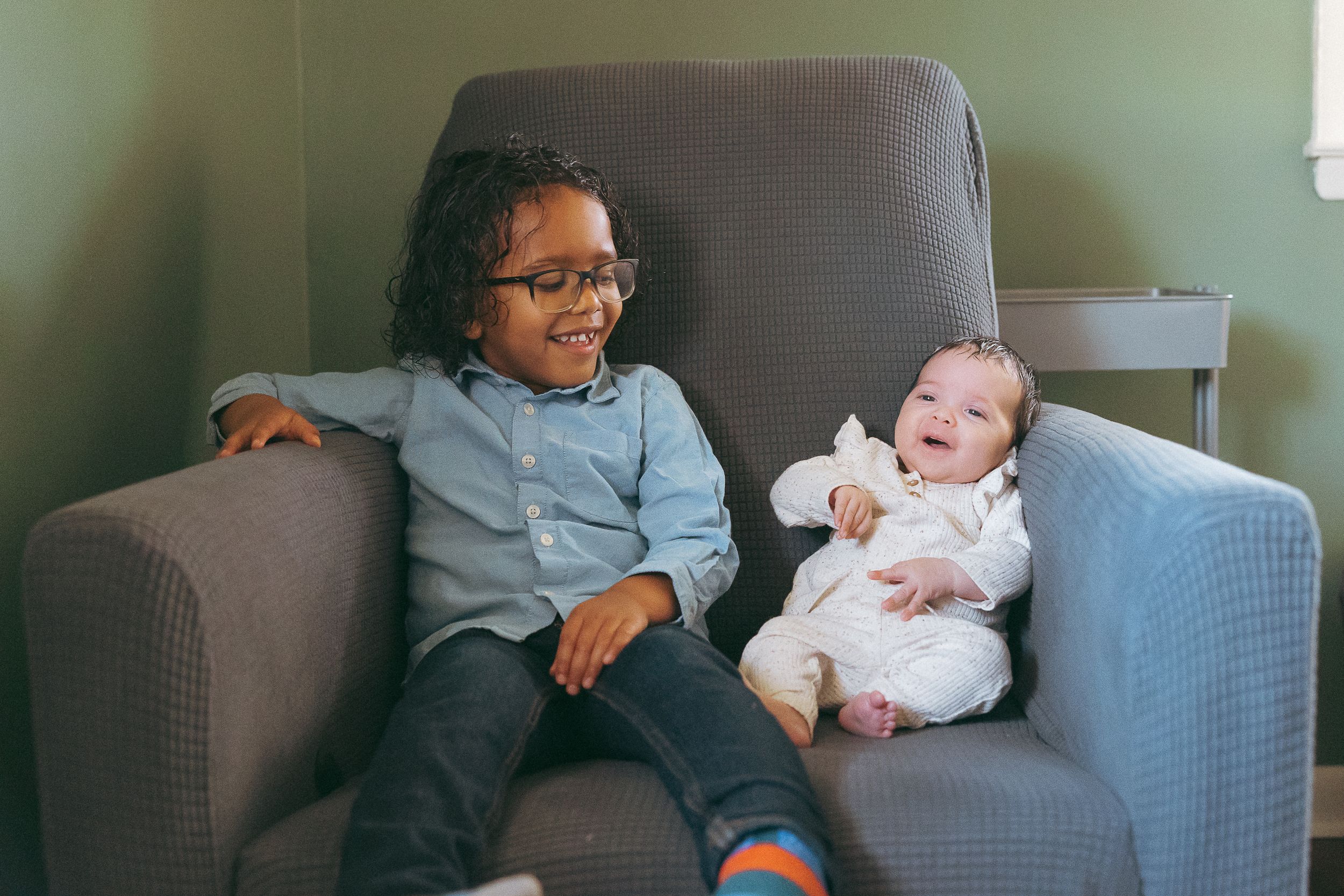 Two young individuals relaxing together on a cozy gray armchair.