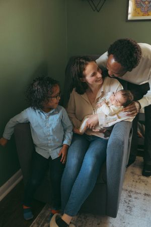 A loving family moment captured in a living room as they huddle together on a dark armchair.