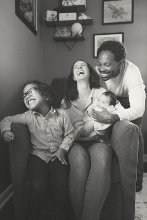 A family shares a joyful moment together on a couch, laughing and bonding while holding a baby.