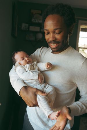 A parent tenderly holds their sleeping newborn baby while wearing a light gray sweater in a dimly lit room.