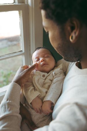 A gentle moment by the window as a baby sleeps peacefully in a cream-colored knit outfit.