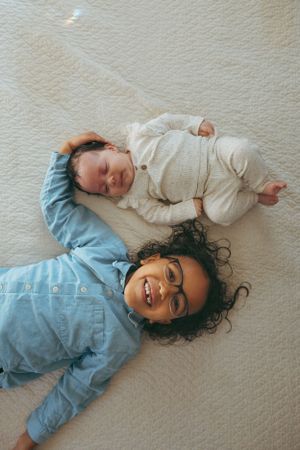 Two people laying on white textured surface with one wearing blue and one wearing cream colored outfits.
