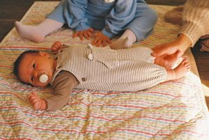 A baby wearing striped overalls lies on a colorful patterned blanket.