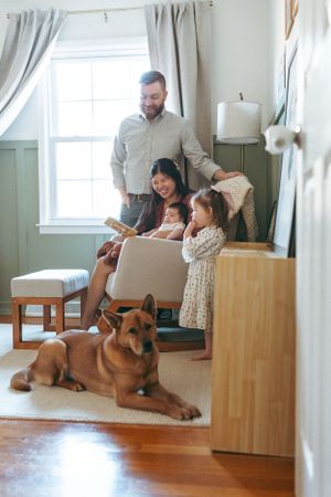A cozy family scene with a German Shepherd dog resting by a window in a warmly lit room.