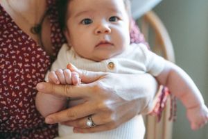 Baby wearing white onesie being held in caregiver's arms with cradled support in close-up view.