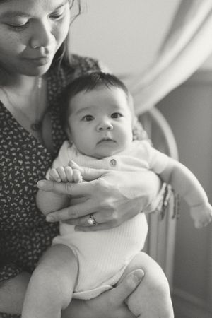 Black and white portrait of baby in white onesie being cradled.