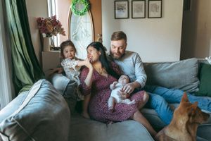 Family relaxing together on a gray couch with a ginger cat while cuddling a baby on a casual afternoon.