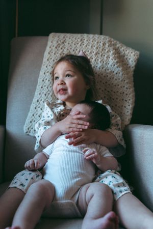 Children sitting together in gray armchair with knit blanket in background.