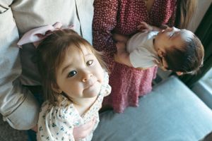 Two siblings lying on a couch, one wearing a floral print top while another sleeps peacefully.